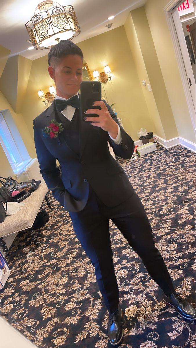 a man in a tuxedo taking a selfie with his cell phone while standing on a carpeted area