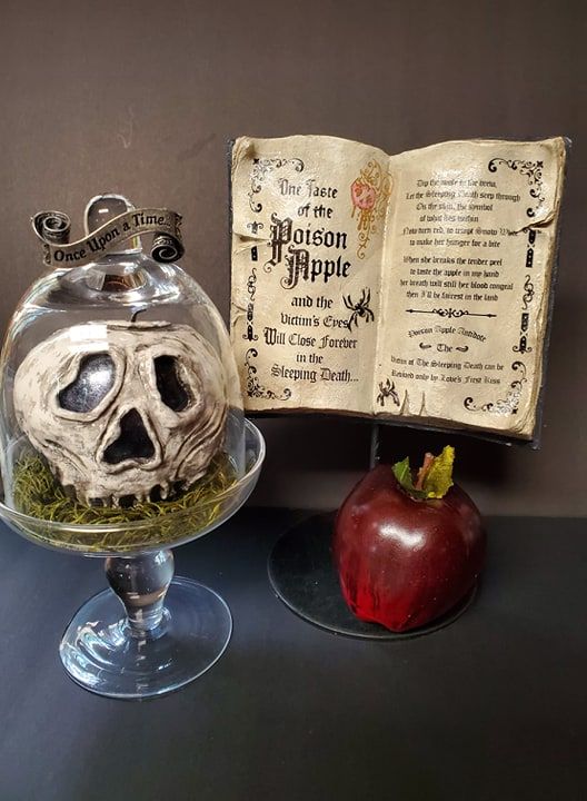 an apple sits next to a glass jar with a fake skull in it and a book on the table