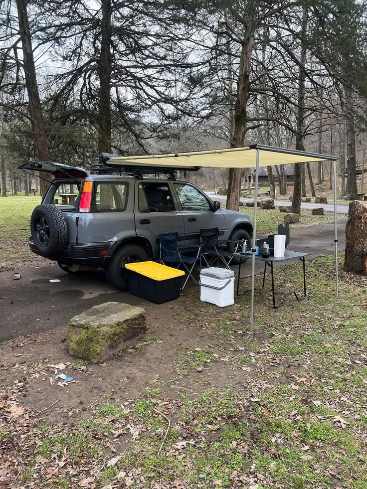 an suv parked next to a picnic table with a tent on it's roof