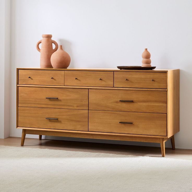 a dresser with two vases on top of it next to a white carpeted floor