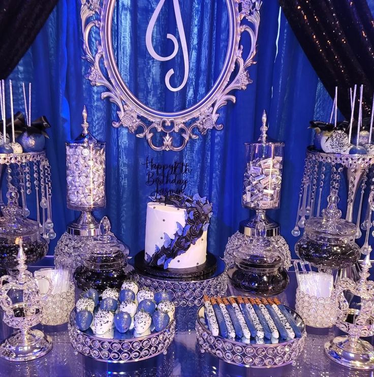 a table topped with lots of desserts and candies next to a blue curtain