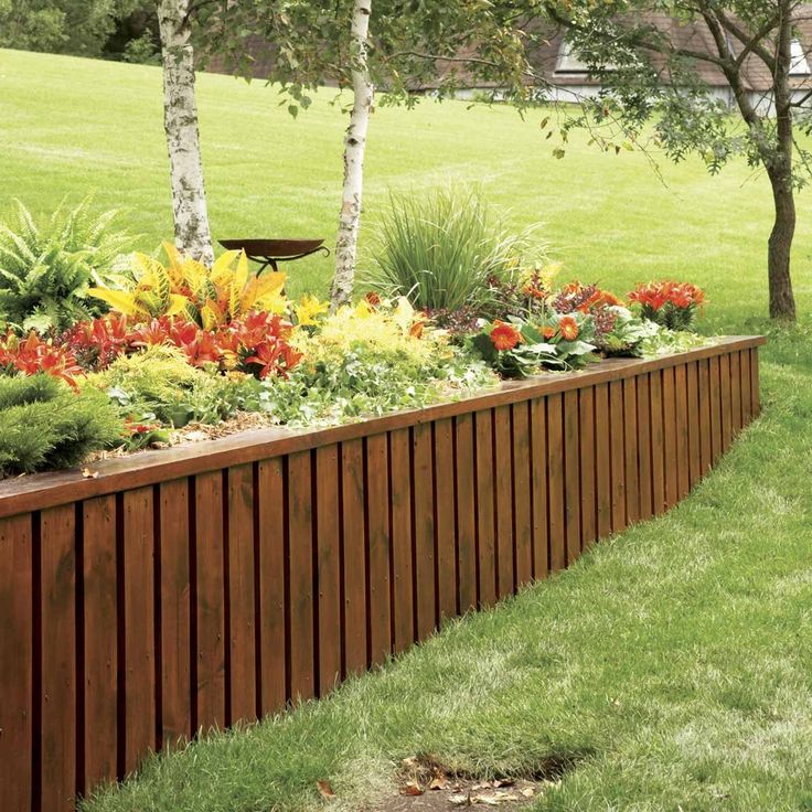 a long wooden planter in the middle of a grassy area with trees and flowers