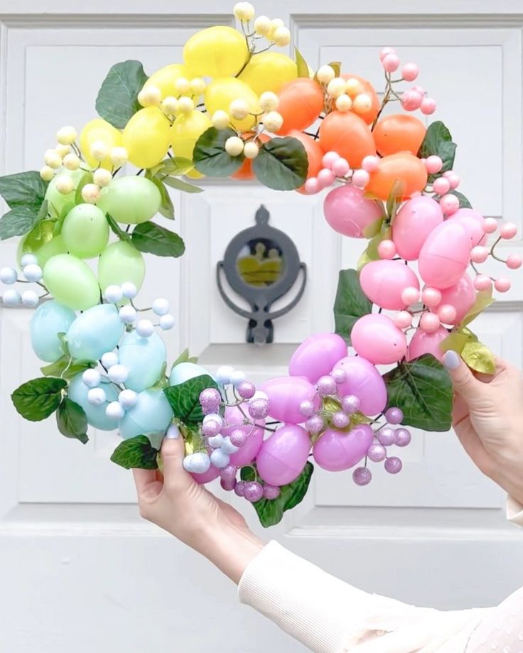 a person holding a wreath made out of fake flowers and leaves in front of a door