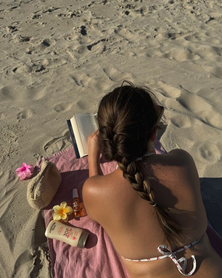 a woman sitting on top of a towel next to an open book