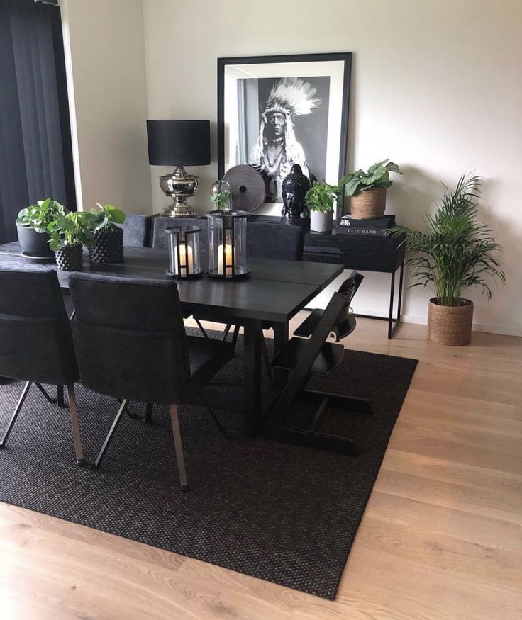 a dining room table with black chairs and plants on the rug in front of it