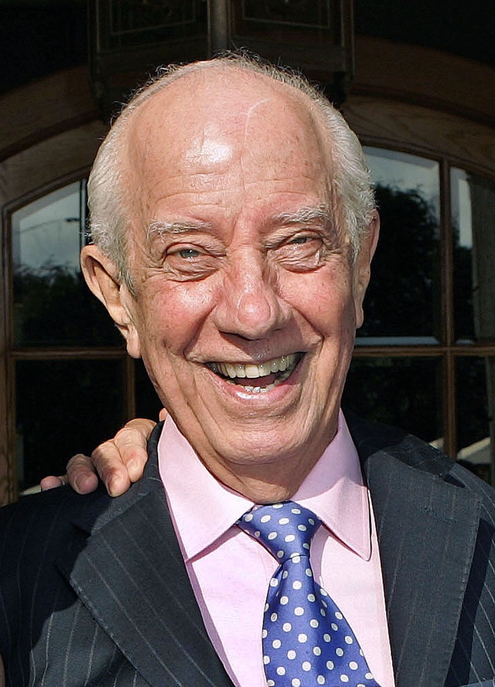 an older man in a suit and tie smiles at the camera with his arm around him