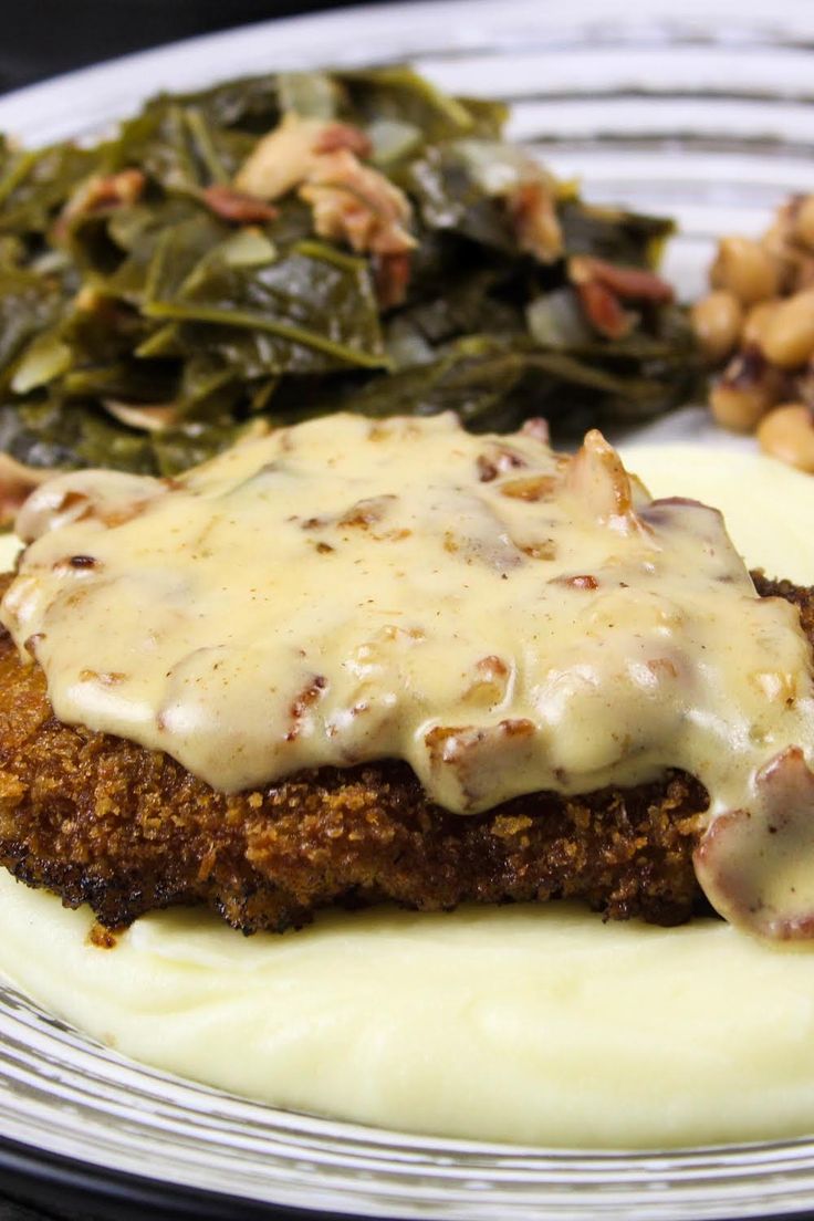 a white plate topped with meat covered in gravy next to potatoes and greens