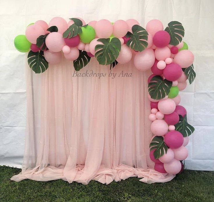 a pink and green balloon arch decorated with monster leaves