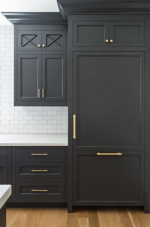 a kitchen with black cabinets and white counter tops, gold pulls on the doors is shown