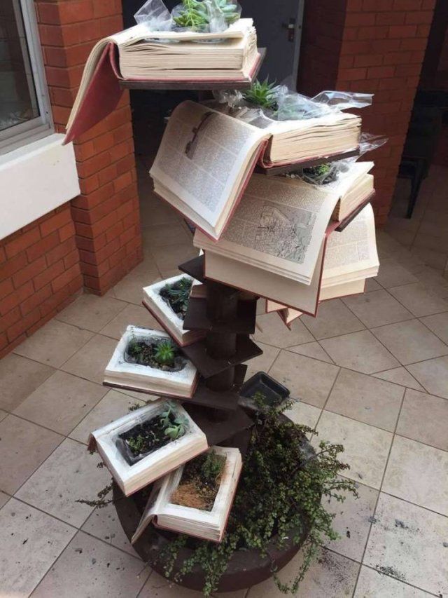 several books are stacked on top of each other in the shape of a tower with plants growing out of them