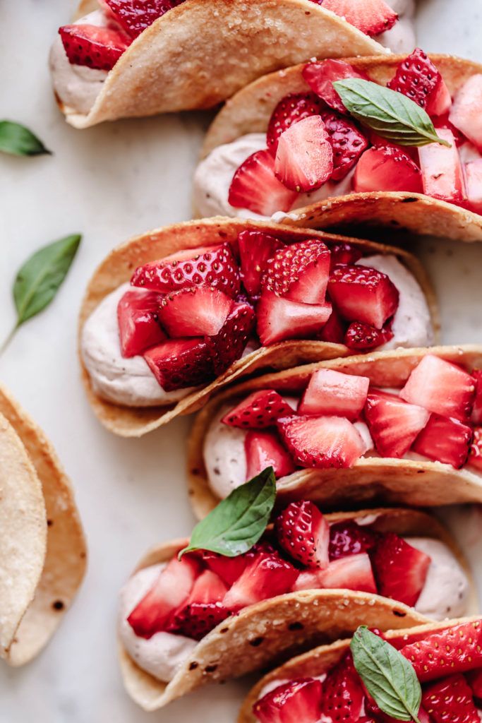 strawberries and whipped cream in tortilla shells on a white surface with green leaves