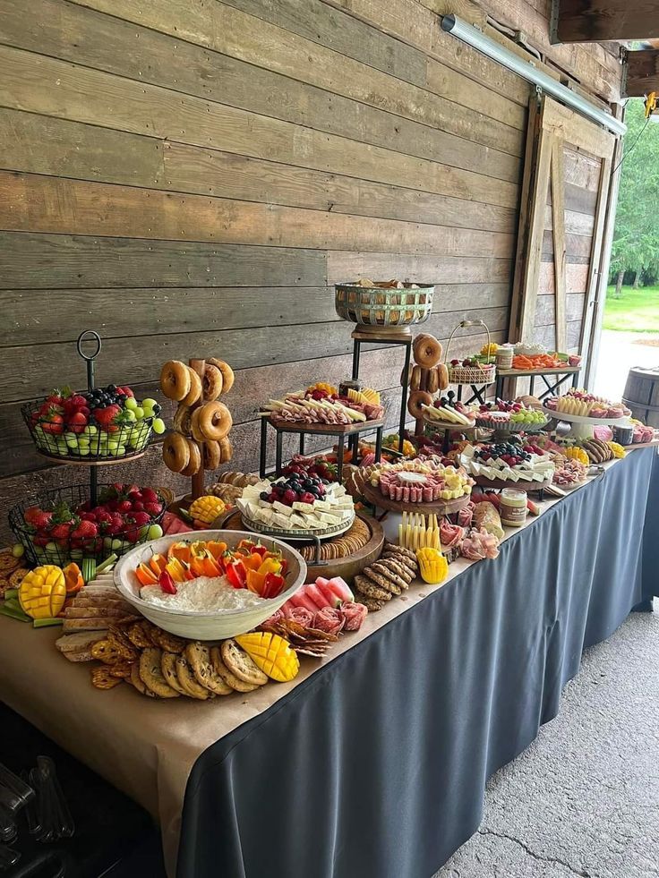 an outdoor buffet with fruits and pastries on the table in front of a wooden wall