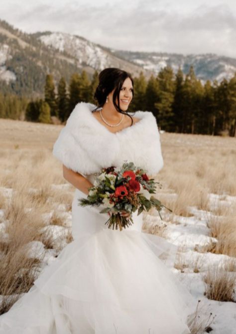 a woman in a wedding dress holding a bouquet and standing in the snow with mountains behind her