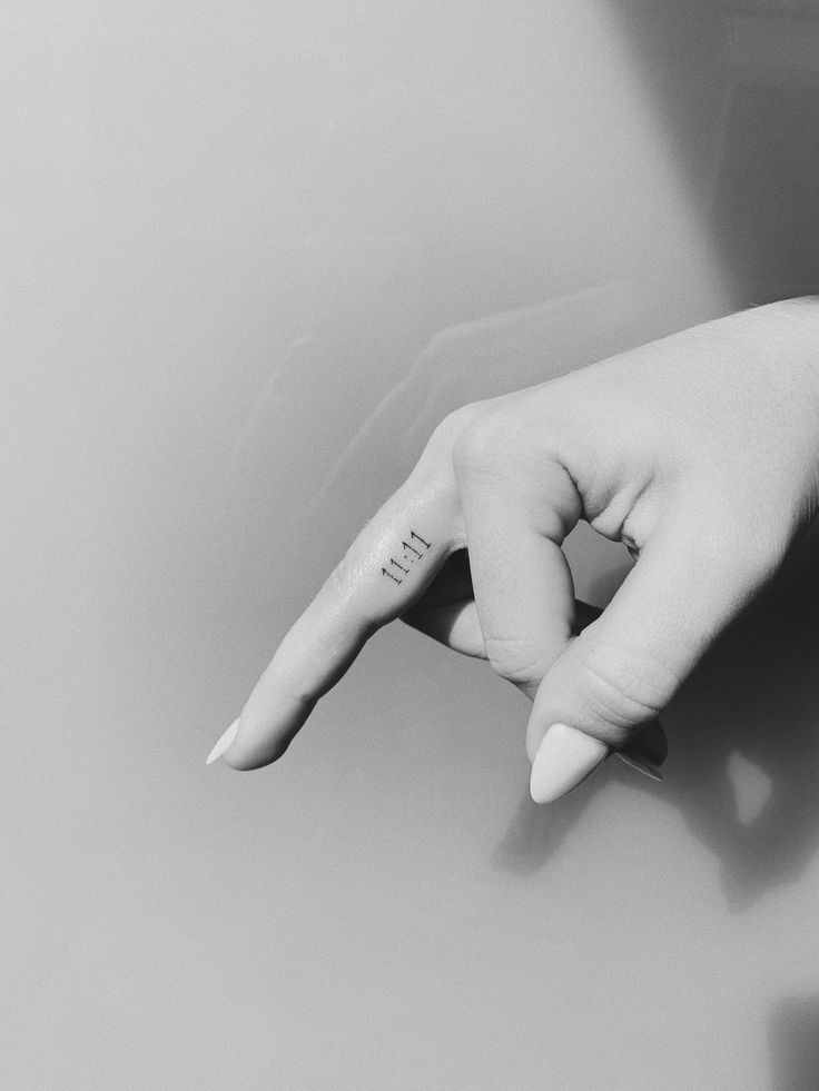 a person's hand with a small tattoo on the middle finger pointing at something