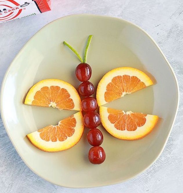 orange slices and grapes are arranged in the shape of a butterfly on a white plate