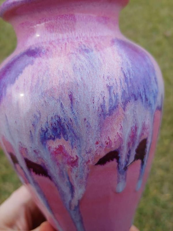 a hand holding a pink and purple vase with blue streaks on it's side