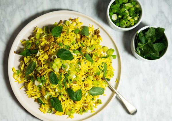 a white plate topped with yellow rice and green vegetables next to two bowls of greens