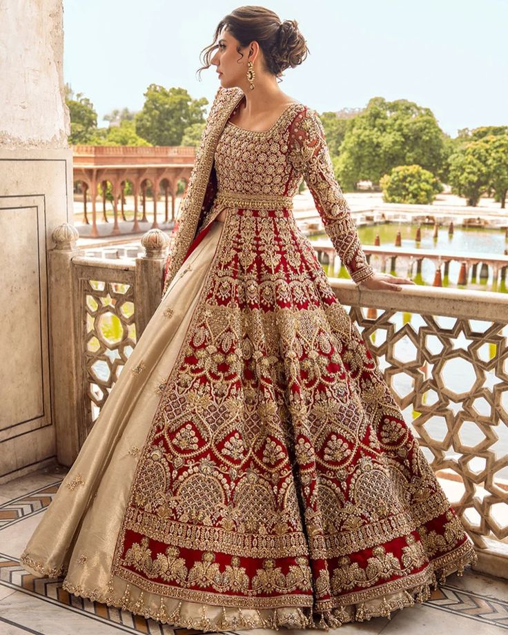 a woman in a red and gold wedding gown standing on a balcony with her hands behind her back