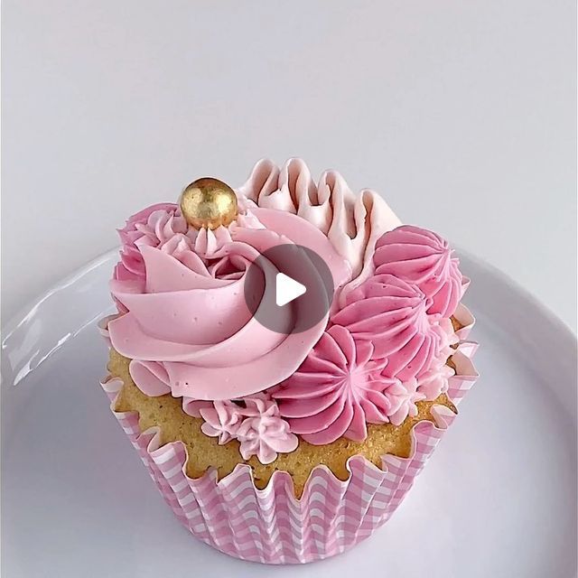 a cupcake with pink frosting and gold decorations on it's top sitting on a white plate