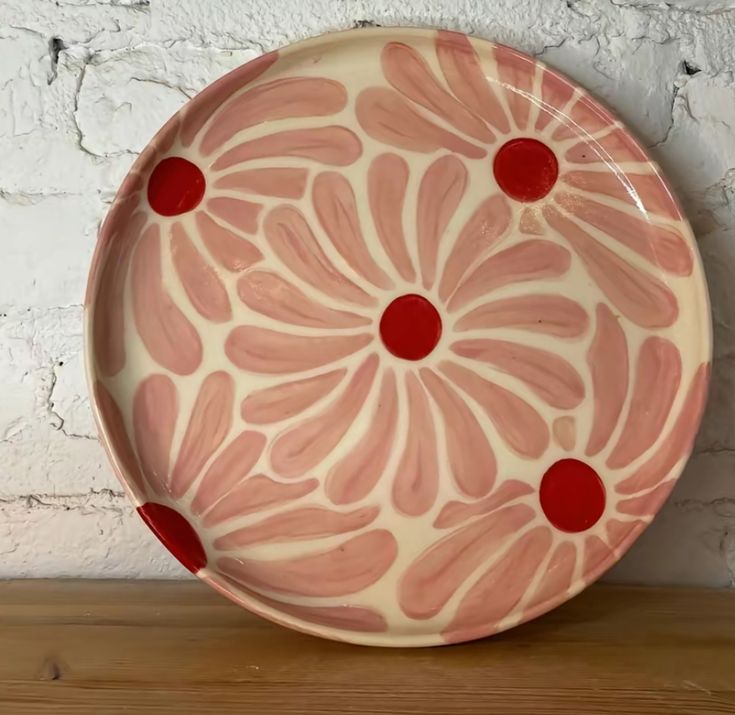 a pink and red plate sitting on top of a wooden table next to a white brick wall