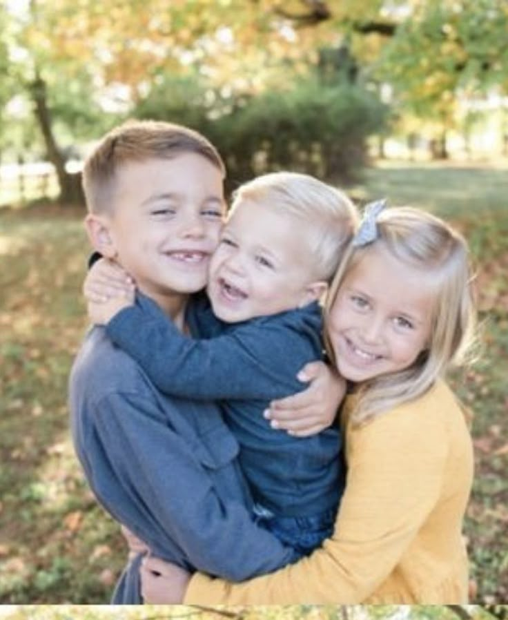 two young children hugging each other in the park with fall leaves on the ground and trees behind them