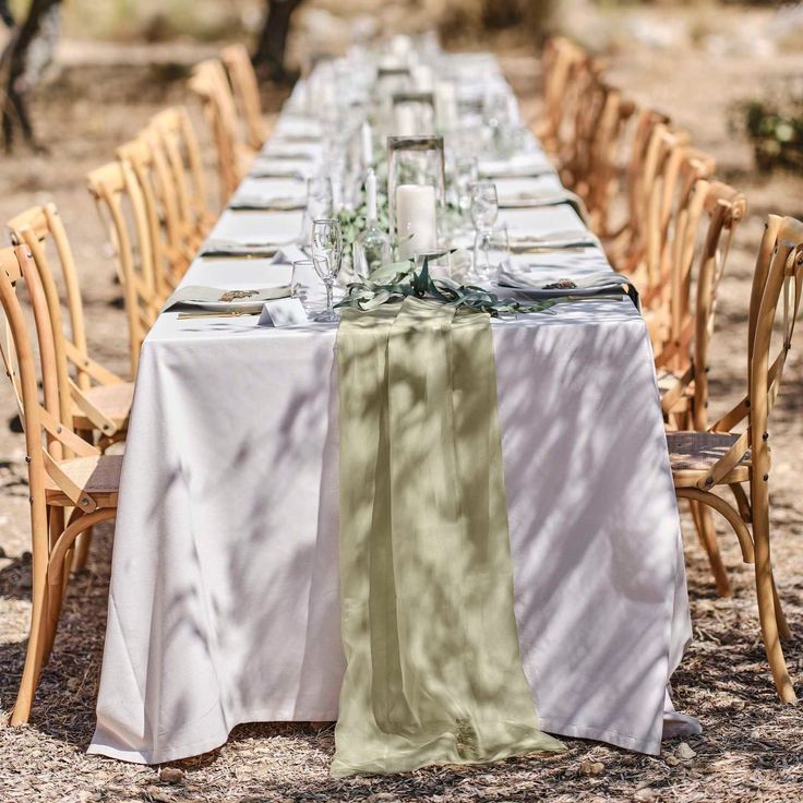 a long table is set up with white and green linens for an outdoor dinner