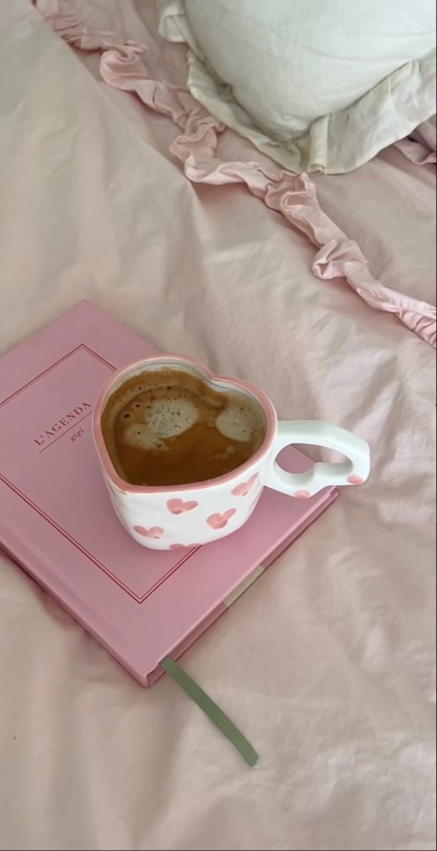 a cup of coffee sitting on top of a pink book next to a white pillow