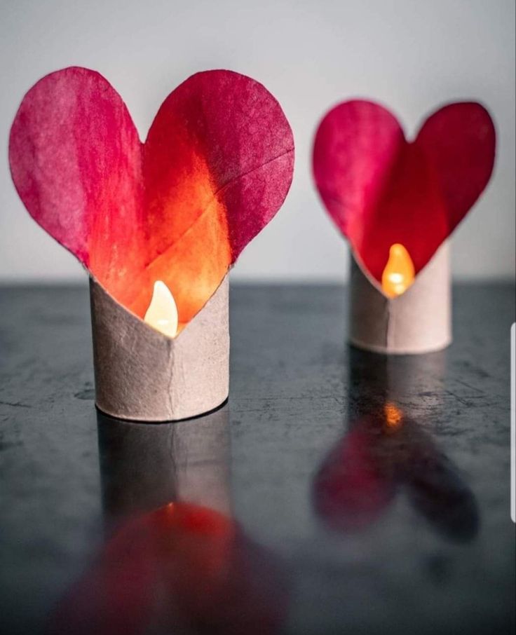 two paper cups with candles in the shape of hearts on top of a black table