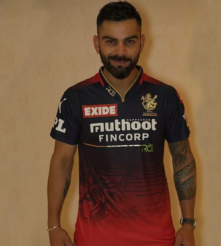 a man with a beard standing in front of a wall wearing a black and red jersey