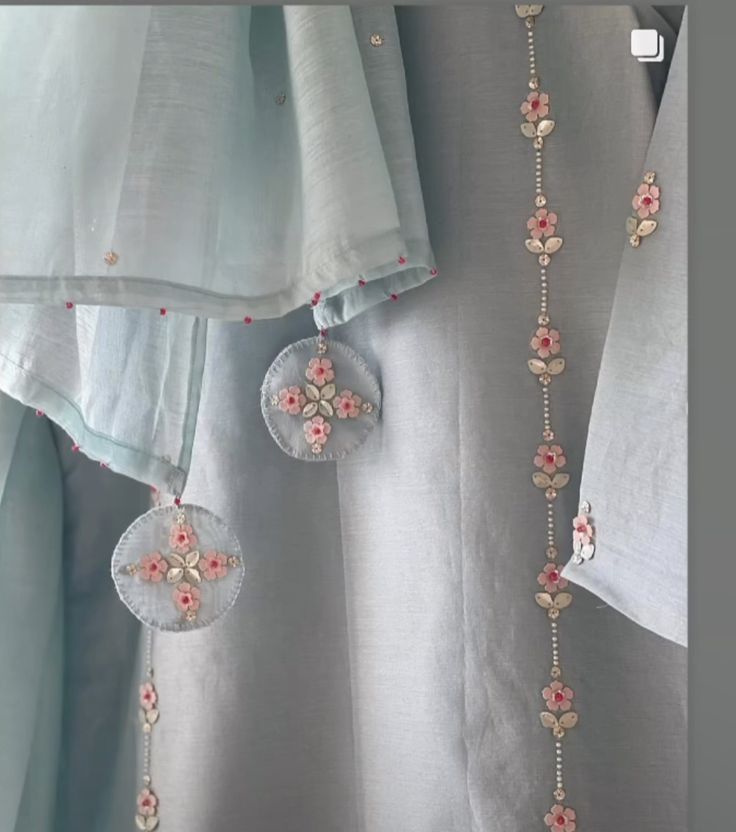 two necklaces hanging from the side of a curtain in front of curtains with flowers on them