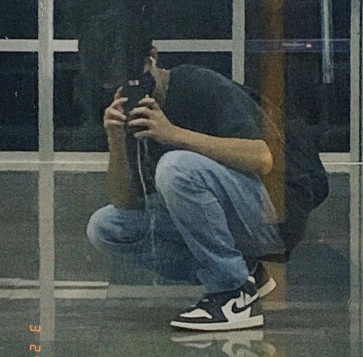 a man squatting on the ground taking a selfie with his cell phone in front of him