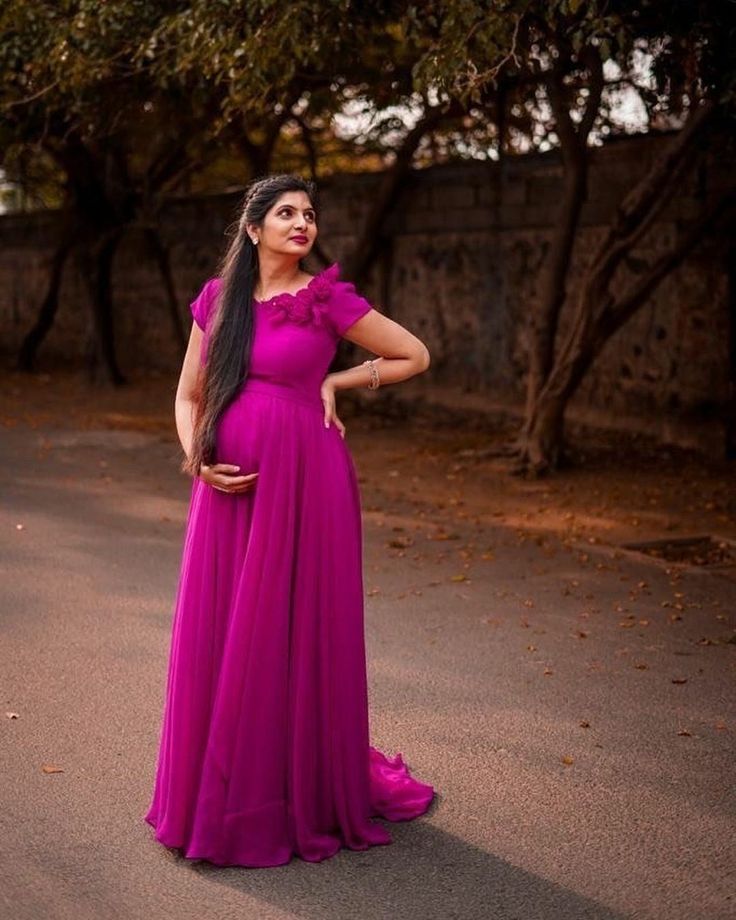 a woman in a long purple dress standing on the street with her hands on her hips