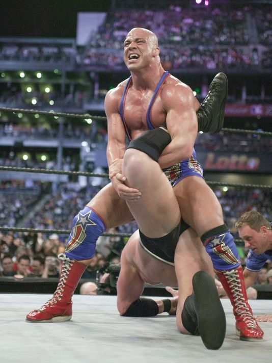 two men wrestling in front of an audience at a sporting event, one is holding the other's leg