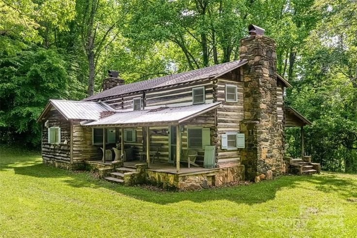 an old log cabin sits in the middle of a grassy area with trees around it