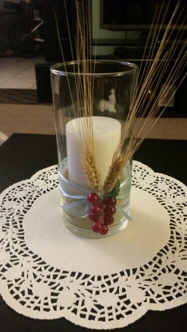 a candle is sitting on a doily next to a glass with wheat stalks in it