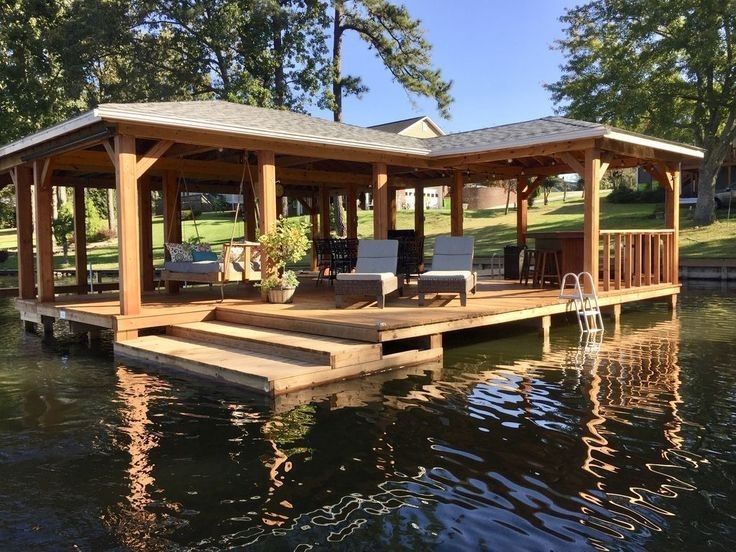 a dock with chairs on it in the middle of a body of water next to a house