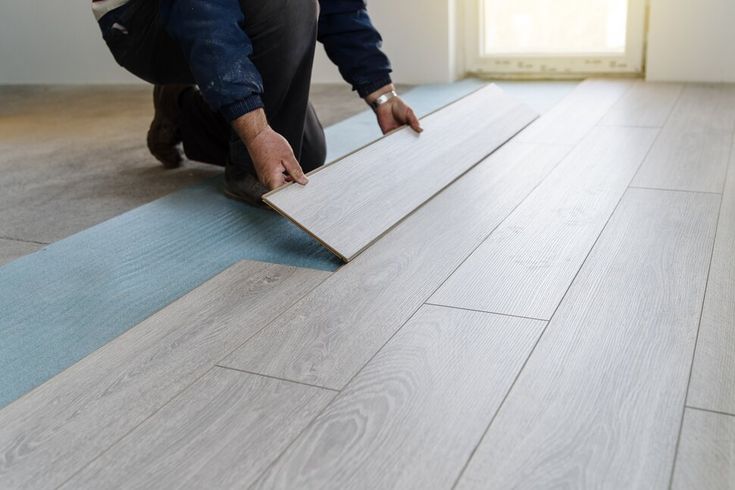 a man laying wood flooring on top of a hard wood floor