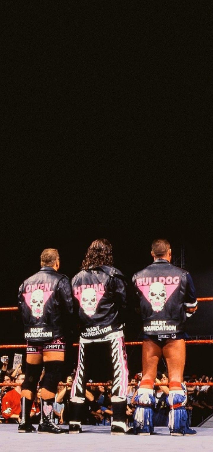 two women in black jackets standing next to each other on a wrestling ring with people watching