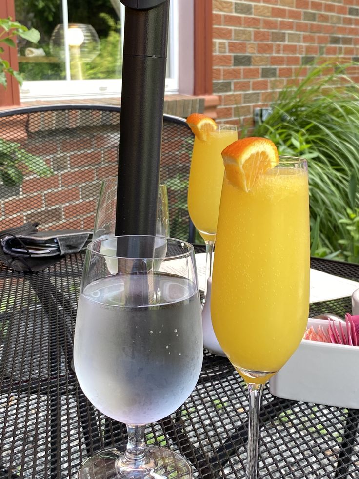 two glasses filled with drinks sitting on top of a table next to an orange slice