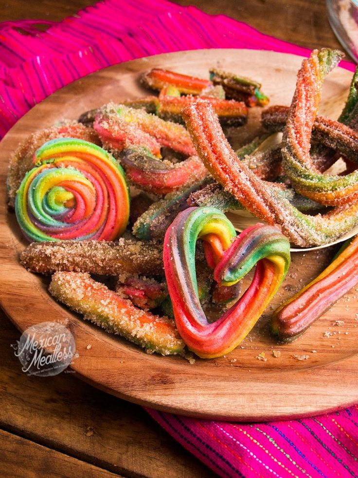 a plate full of colorful candy canes on top of a pink table cloth next to a spoon