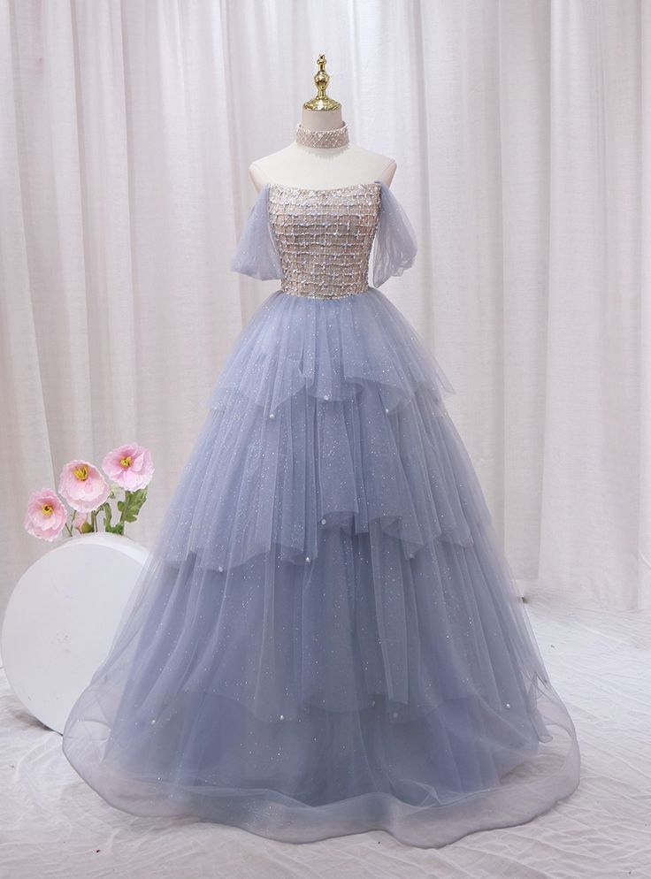 Admire this ethereal blue prom dress, a dream in tulle and sparkle! Fashioned to enchant, this gown features a shimmering, sequined bodice that catches every light, matched with an off-the-shoulder neckline that exudes elegance. The bodice seamlessly transitions into a multi-layered tulle skirt, adorned with delicate sparkles that mimic distant stars in the night sky. Each layer cascades in a gentle flurry, adding volume and a fairy-tale finish to this magnificent dress. Perfect for a prom or any special occasion, this dress guarantees you'll float through the evening with grace and poise. The soft blue hue complements every skin tone, ensuring that you look picture-perfect for every photo opportunity. Fairytale Dress Prom, Ethereal Blue, Gold Tulle, Photo Opportunity, Blue Prom Dress, Prom Dress Plus Size, Strapless Prom Dress, Layered Tulle Skirt, Prom Dresses Two Piece