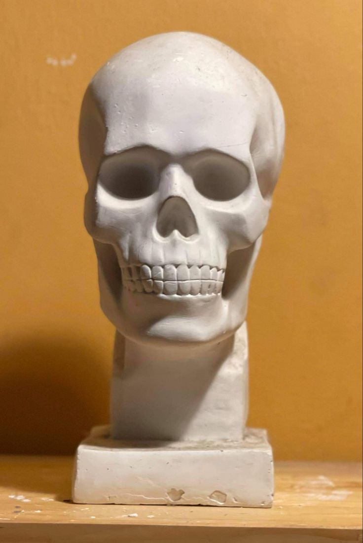 a white skull statue sitting on top of a wooden table next to a yellow wall