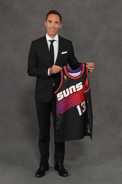 a man in a suit and tie holding up a suns jersey with the number 13 on it