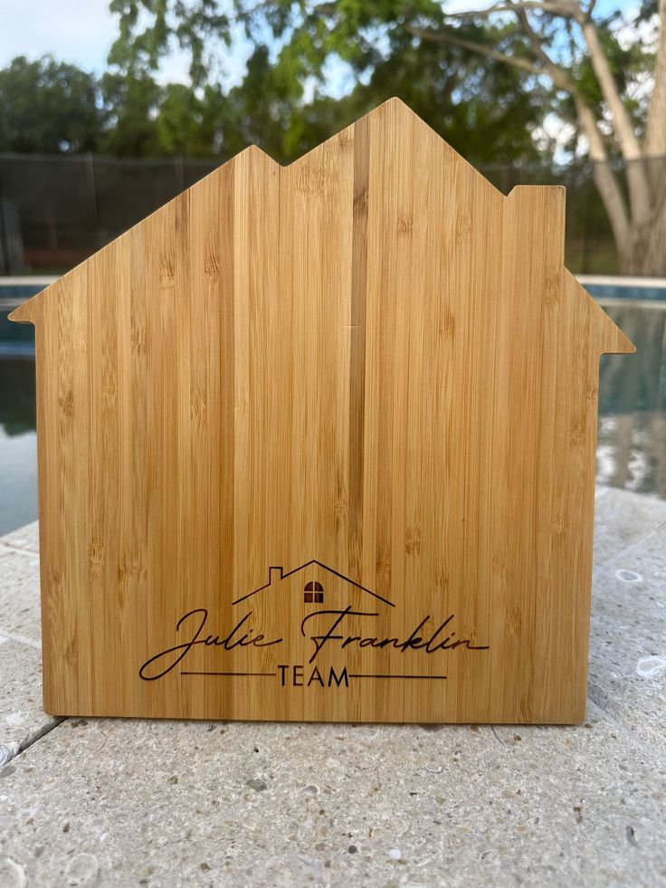 a house shaped cutting board sitting on top of a stone slab next to a pool