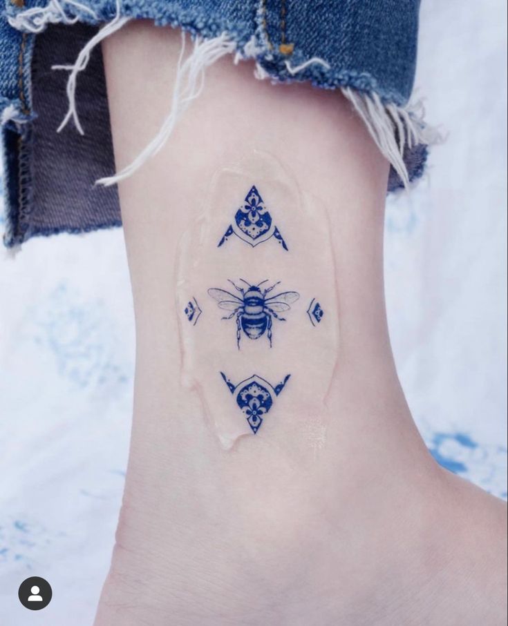 a small tattoo on the ankle of a woman's foot with blue and white designs