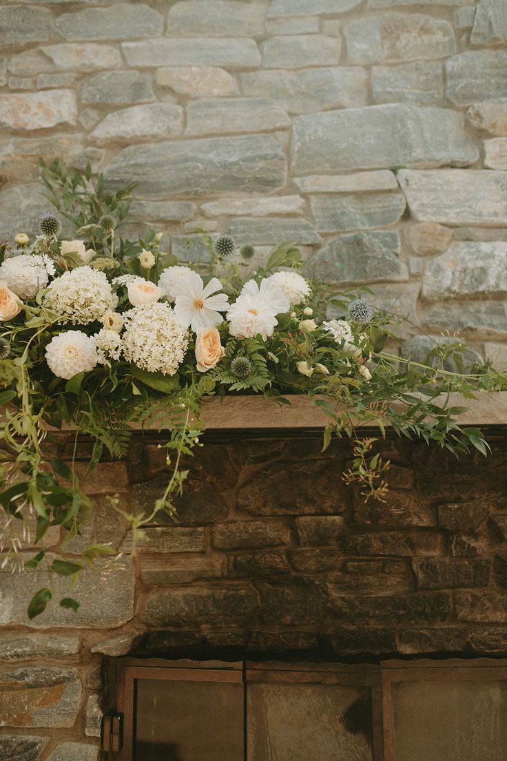 white flowers are sitting on top of a stone fireplace mantel in front of a brick wall