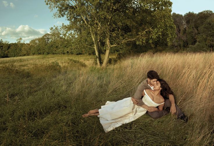 a man and woman are sitting in the tall grass with their arms around each other