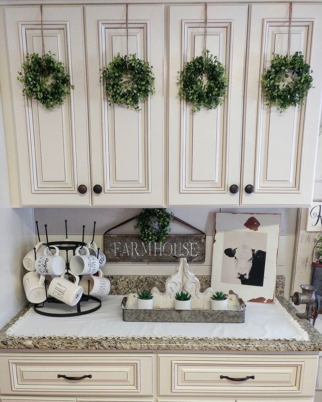 a kitchen with white cabinets and green wreaths on the wall above the counter top