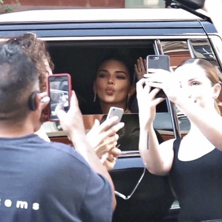 two women are taking pictures in the back of a van while another woman is holding up her cell phone