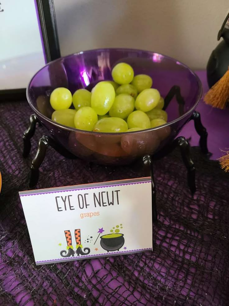 a purple bowl filled with green grapes next to a sign that says eye of neut